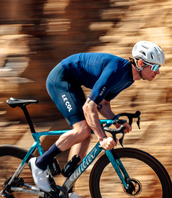Male cyclist in navy jersey, with a blurred background of a rockface along the roadside.