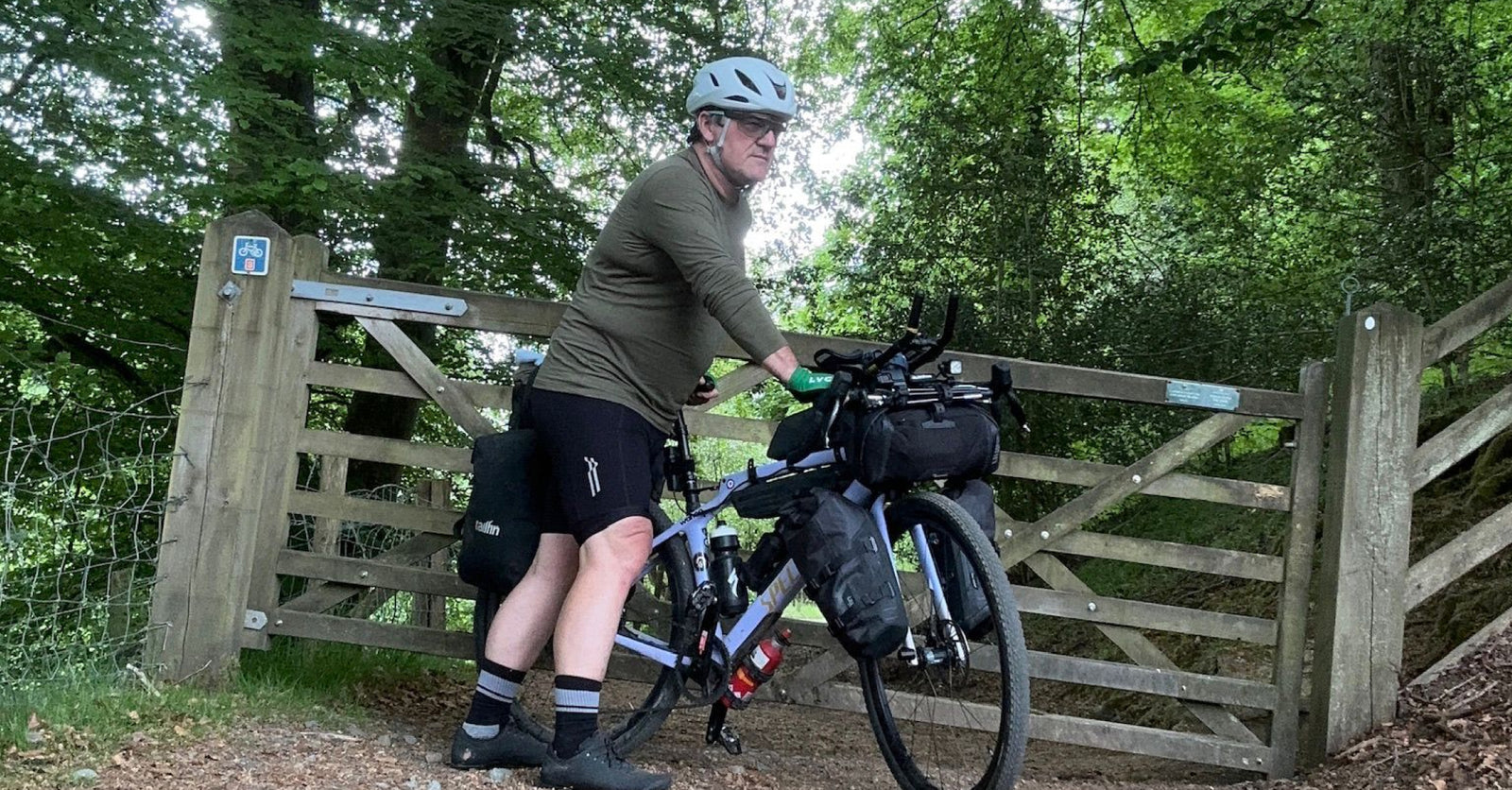 Stephan stood with his bike by a wooden gate in woodlands