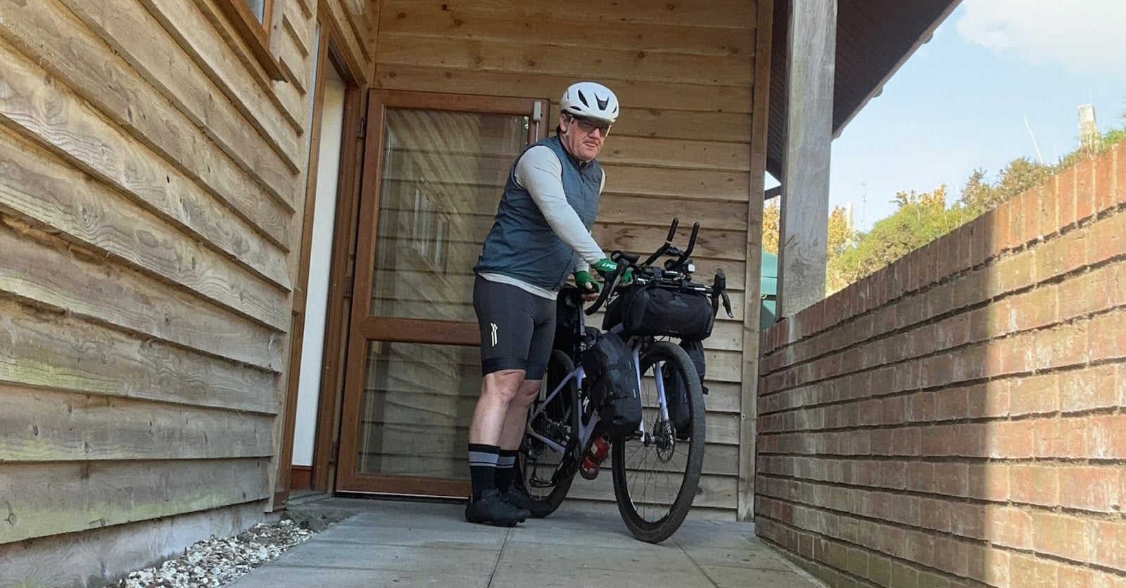 Stephan in Le Col's ARC bibshorts with loaded bike outside a wooden clad building