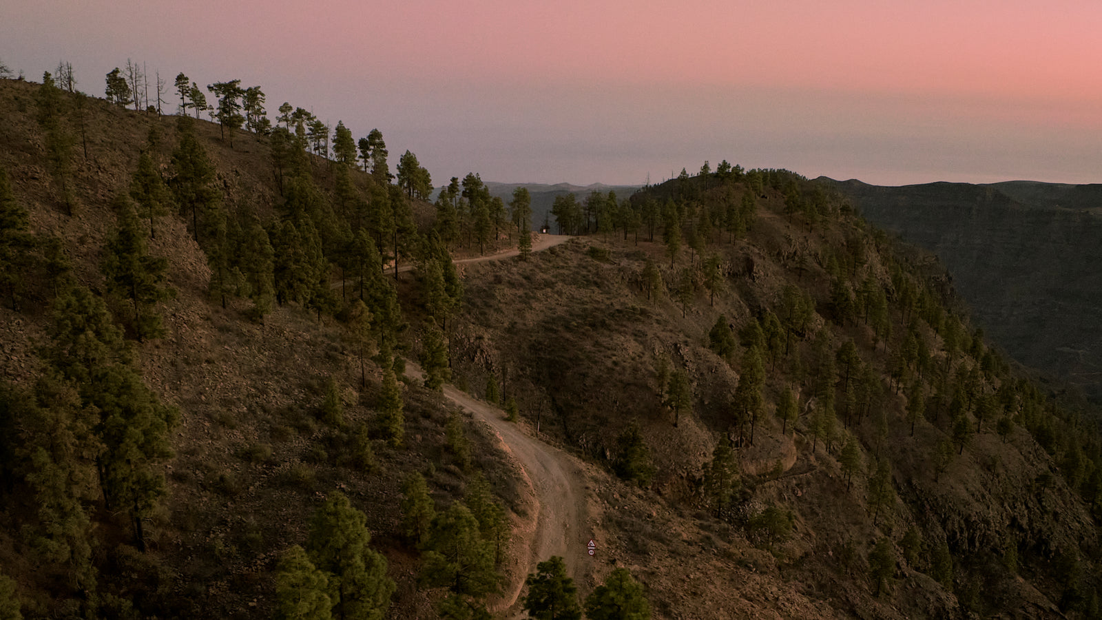 Landscape shot of gravel track along the side of tree dotted mountain.