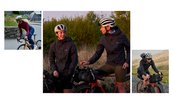 two female cyclists paused on their bikes in jackets with shrubs behind.