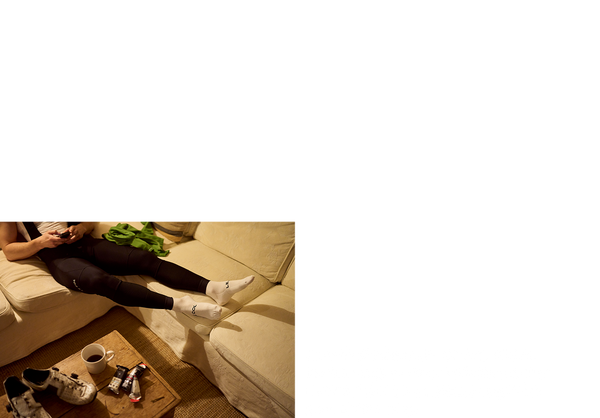 Man on a sofa in a baselayer and bib tights checking his route on his phone.