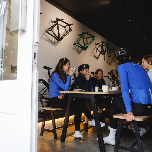 Group of female cyclists sat around a cafe table.