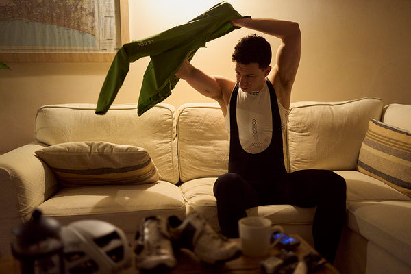 Man putting on long sleeve jersey sat on a sofa.