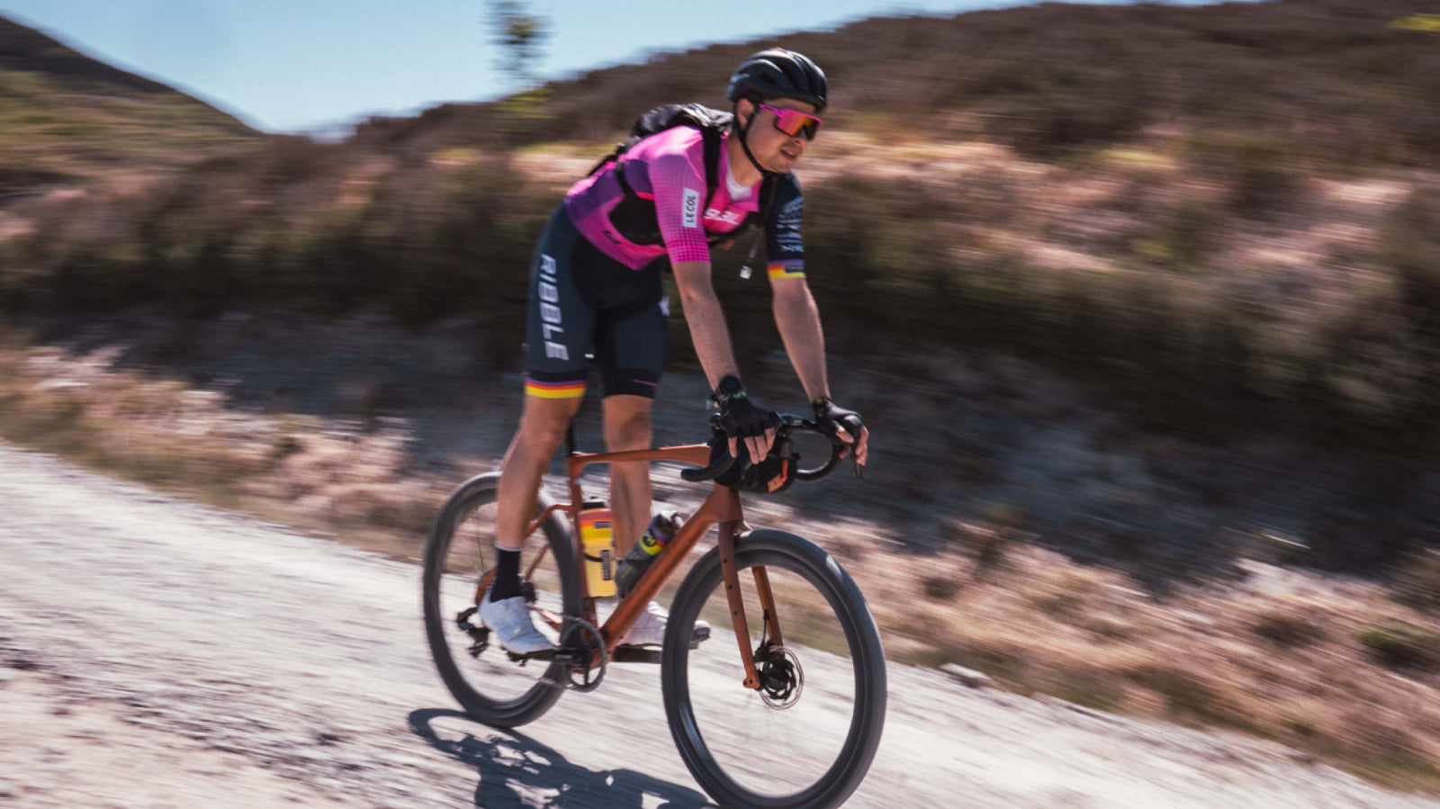 Ribble cyclist in a pink and black outfit riding a bicycle with a scenic background.