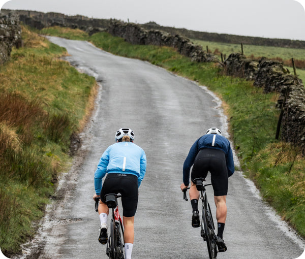 Two cyclists riding away uphill on a stone wall lined road
