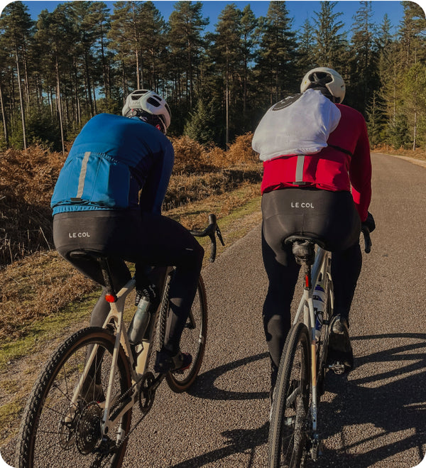 Two cyclists riding away in long sleeve jerseys in a forest