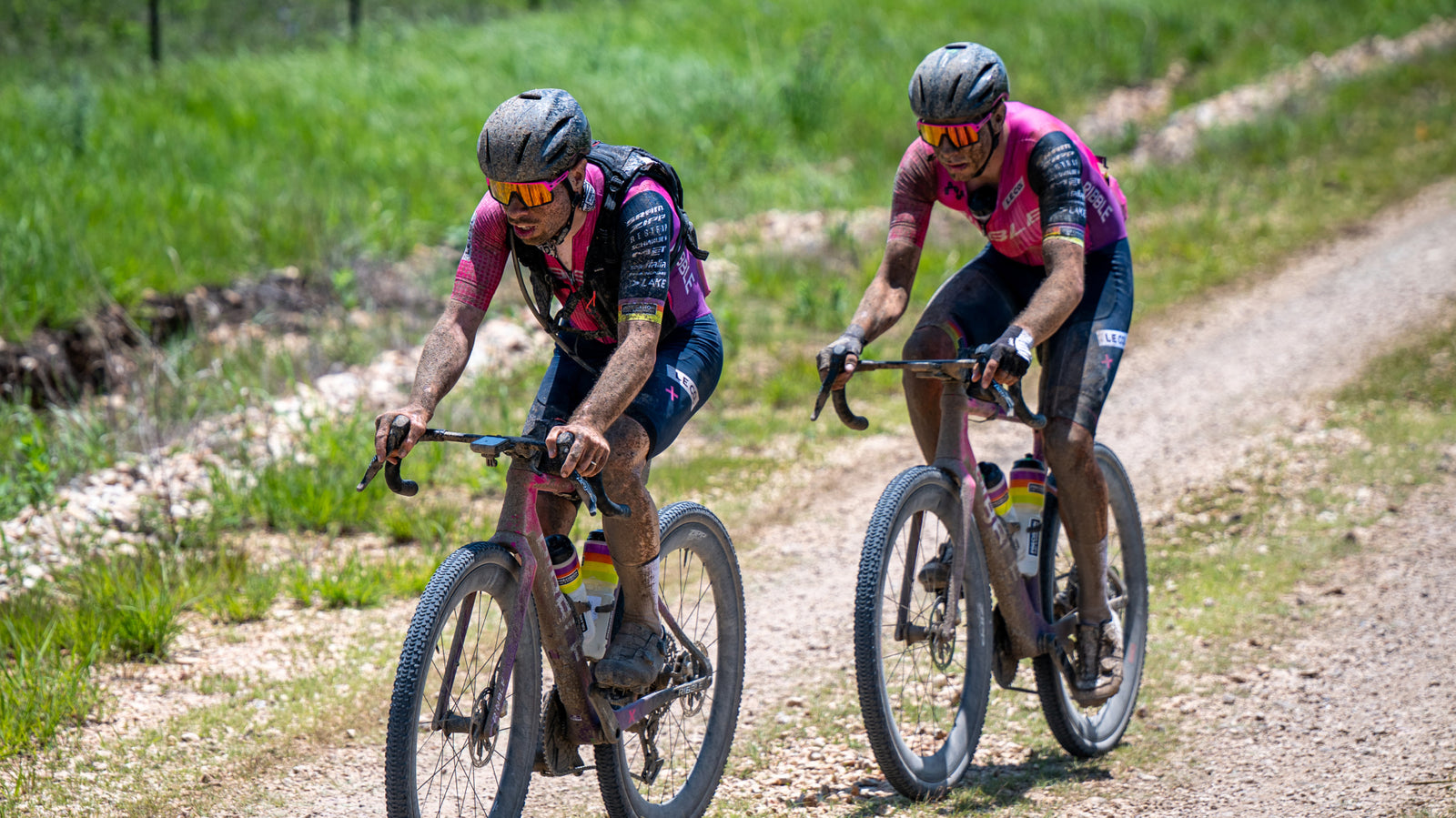 Two Ribble cyclists in pink jerseys riding on a gravel path