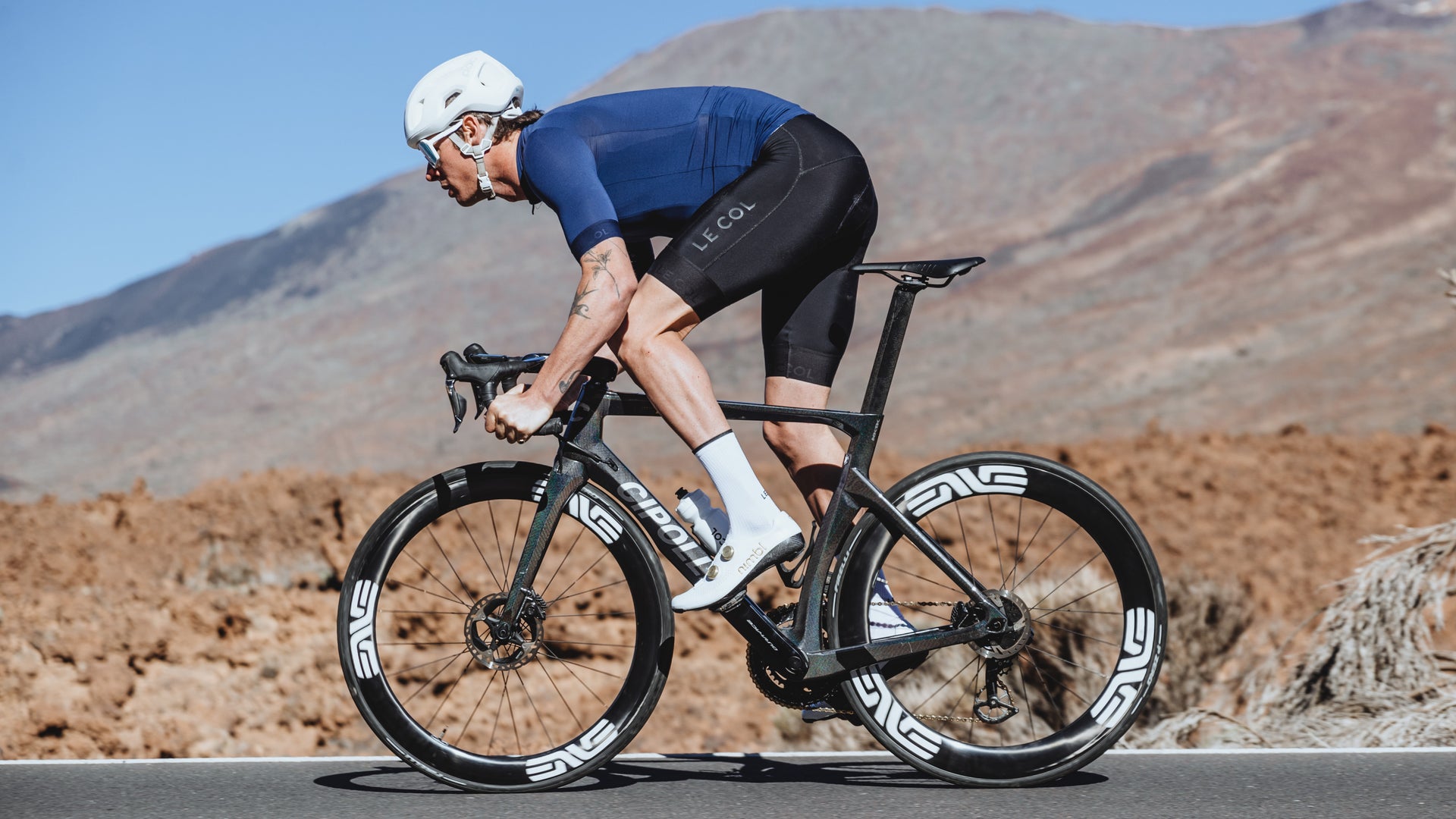 Side profile male cyclist in navy jersey and black bibshorts with rocky mountain background