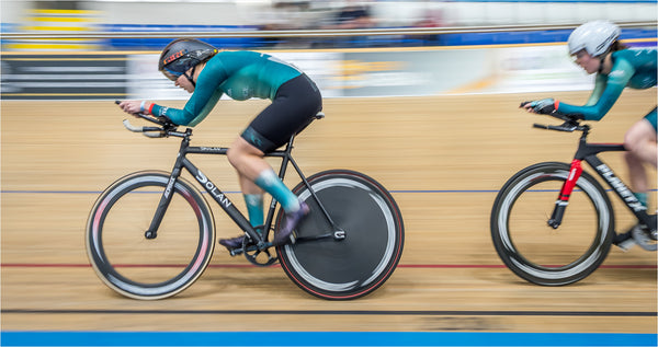 Two female cyclists in Cambridge blue jerseys racing in a velodrome