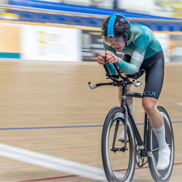 Male cyclist in Cambridge blue jersey racing in a velodrome