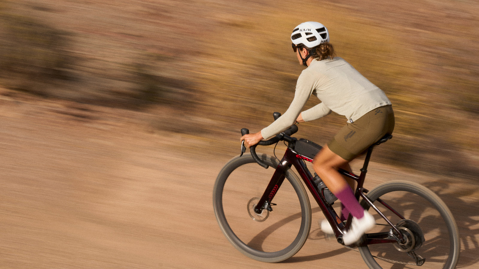 Female rider in stone long sleeve top and brown bibshorts with blurred background.