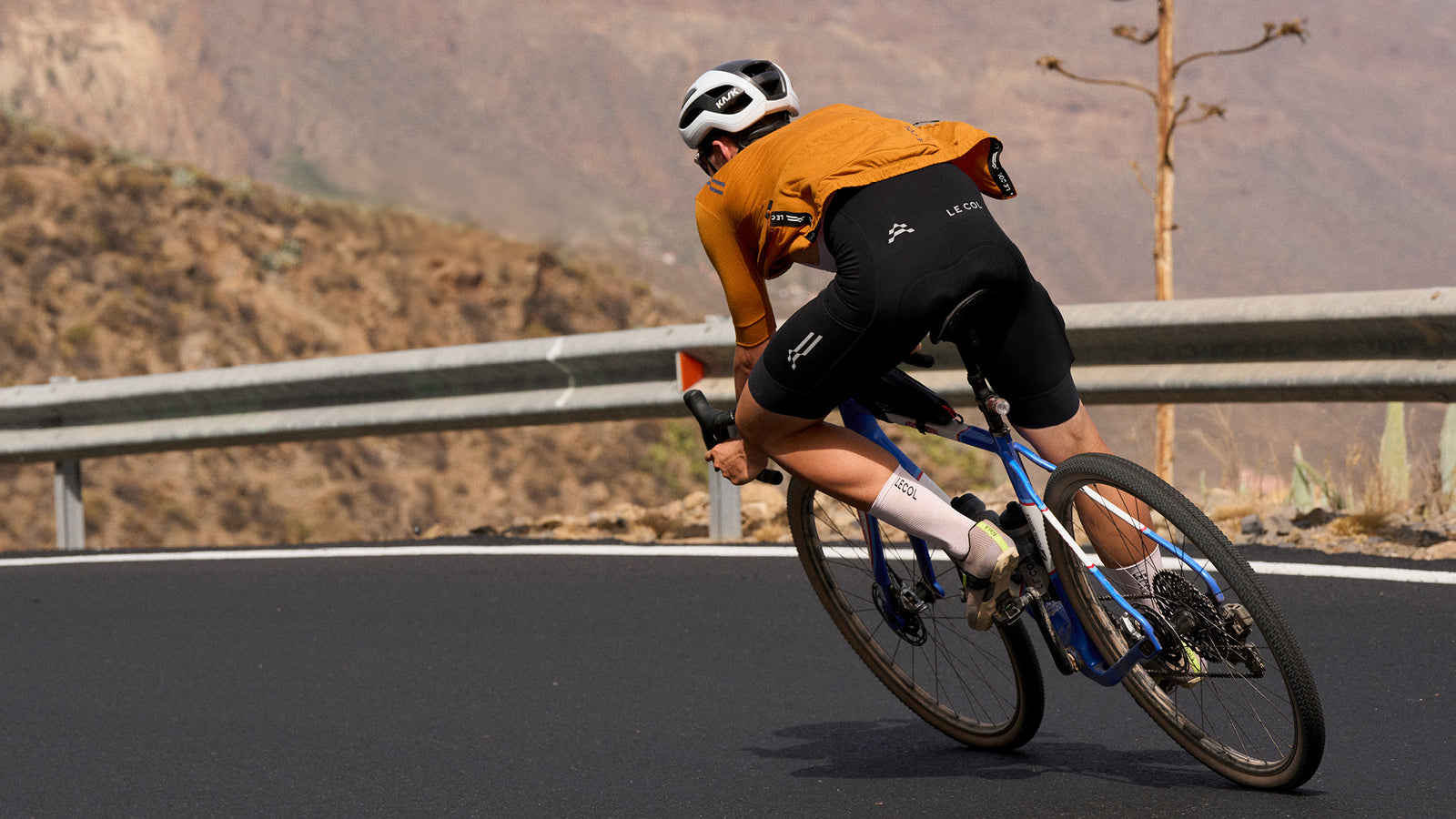 Male rider going away downhill on mountain road in amber jersey.