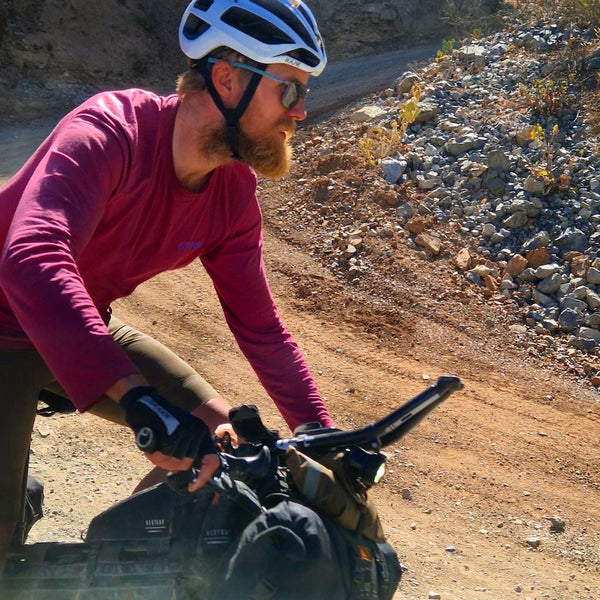 Close up of Angus cycling in Le Col merino t-shirt riding round a dirt track bend.