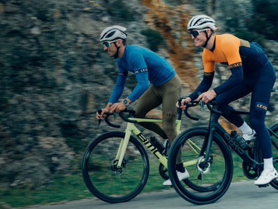 Two cyclists riding on a road with a blurred background.