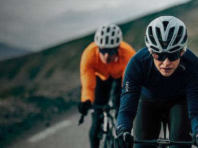 Two cyclists on a road with a mountainous background