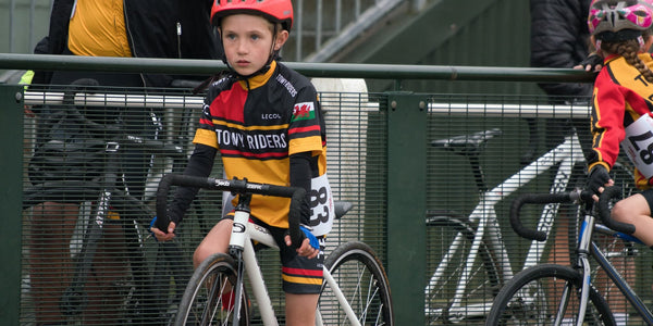 Two children waiting to cycle in a race, one in Le Col kit.