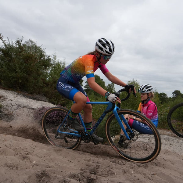 Young female cyclist on a sandy track with bushes in the background.