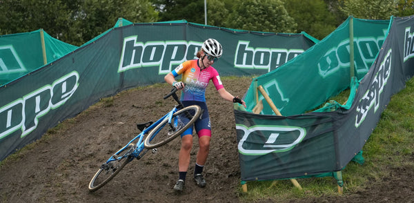 Young female cyclist pulling her bike round a muddy down hill bend in the race.