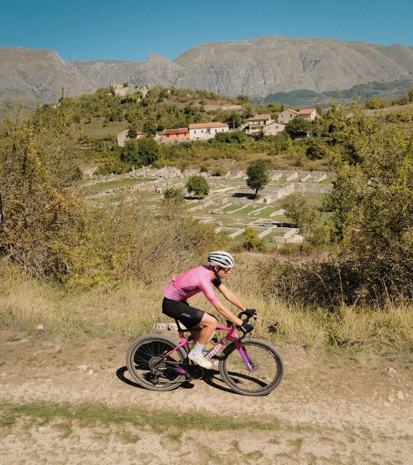 Cyclist in Ribble kit with ancient ruins downhill in the background. 