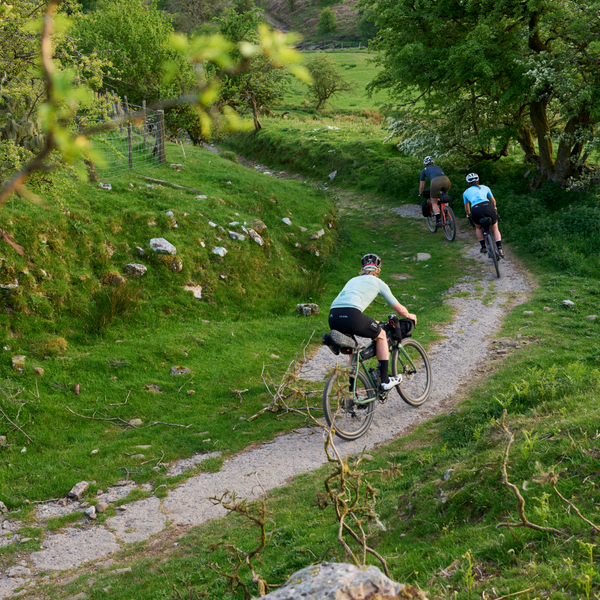 Three riders going downhill away through grassy banks either side
