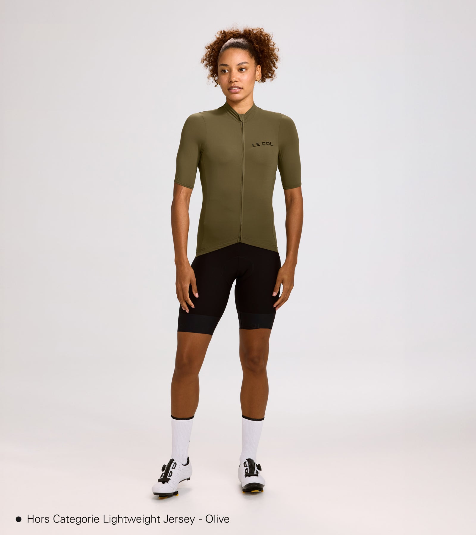 Studio shot of woman wearing an olive green jersey and black bibshorts.