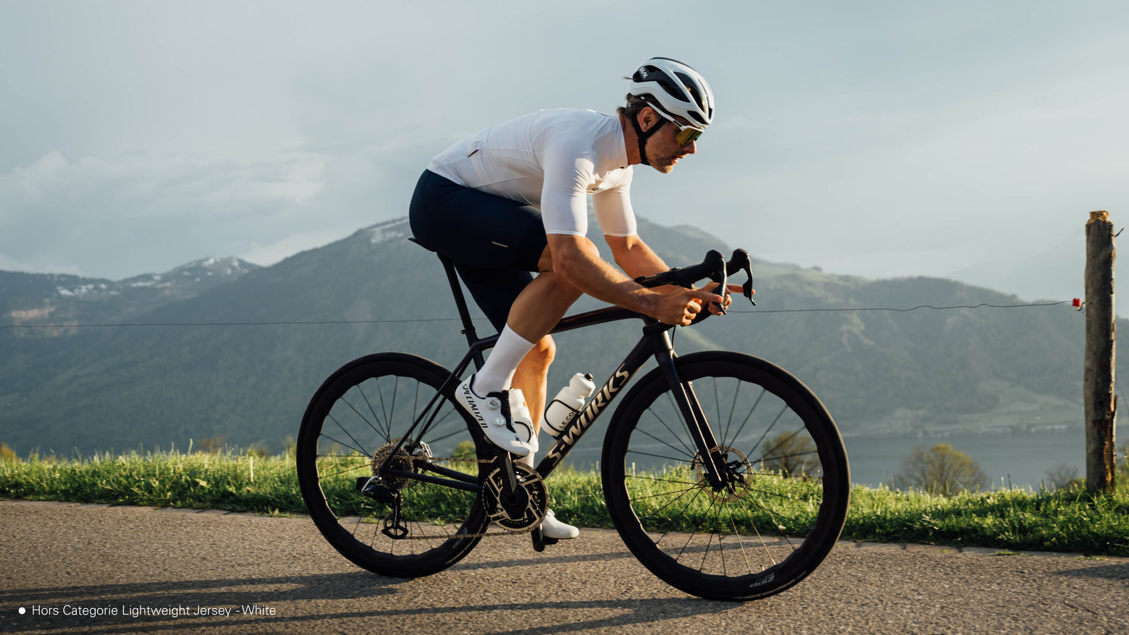 Male cyclist riding in white jersey on a road with mountains in the background
