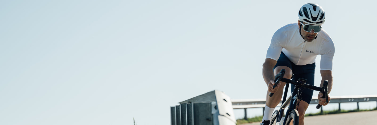 Cyclist in white jersey and black shorts riding a bicycle on a clear day.