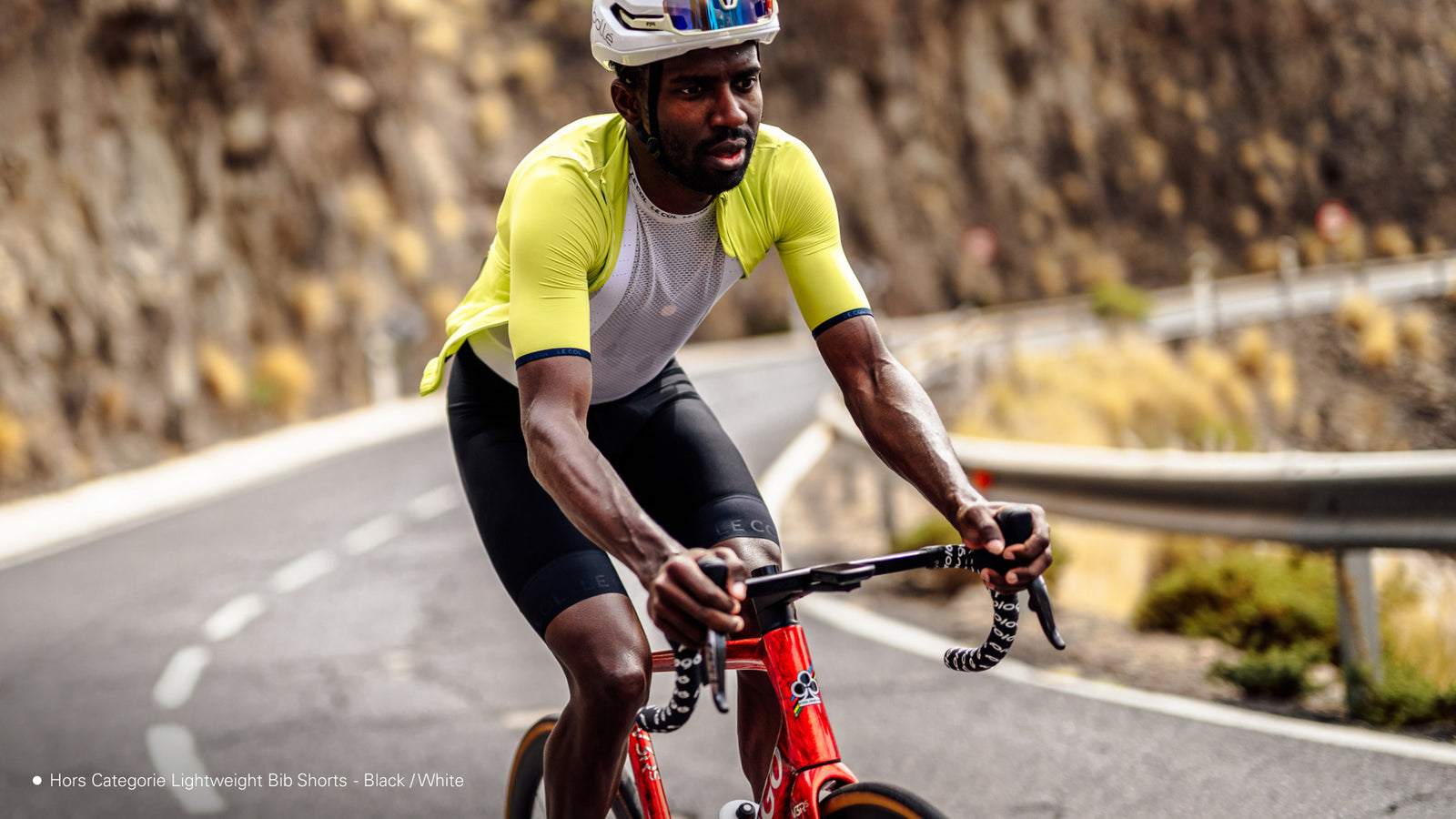 Male cyclist on a mountainside road, in a yellow jersey and black bib shorts