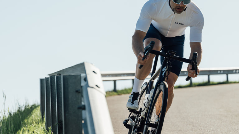 Cyclist in white jersey and black shorts riding a bicycle on a clear day.
