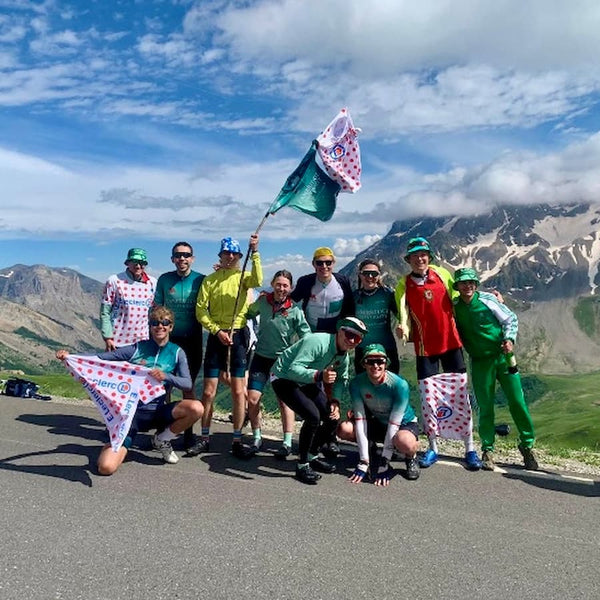 Group photo of cyclists on the roadside with mountains behind.
