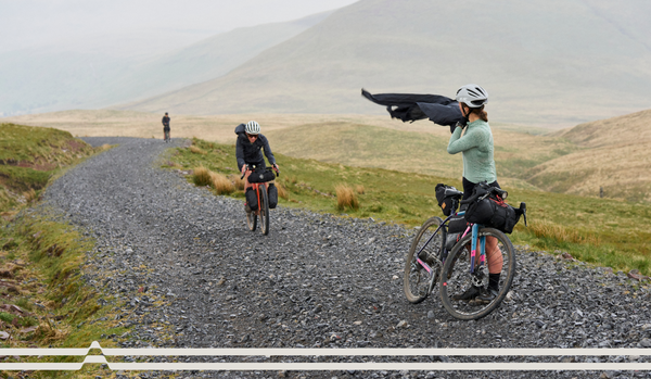 Upland landscape of three riders on a rocky path, one stopped to put on an ARC rain jacket.