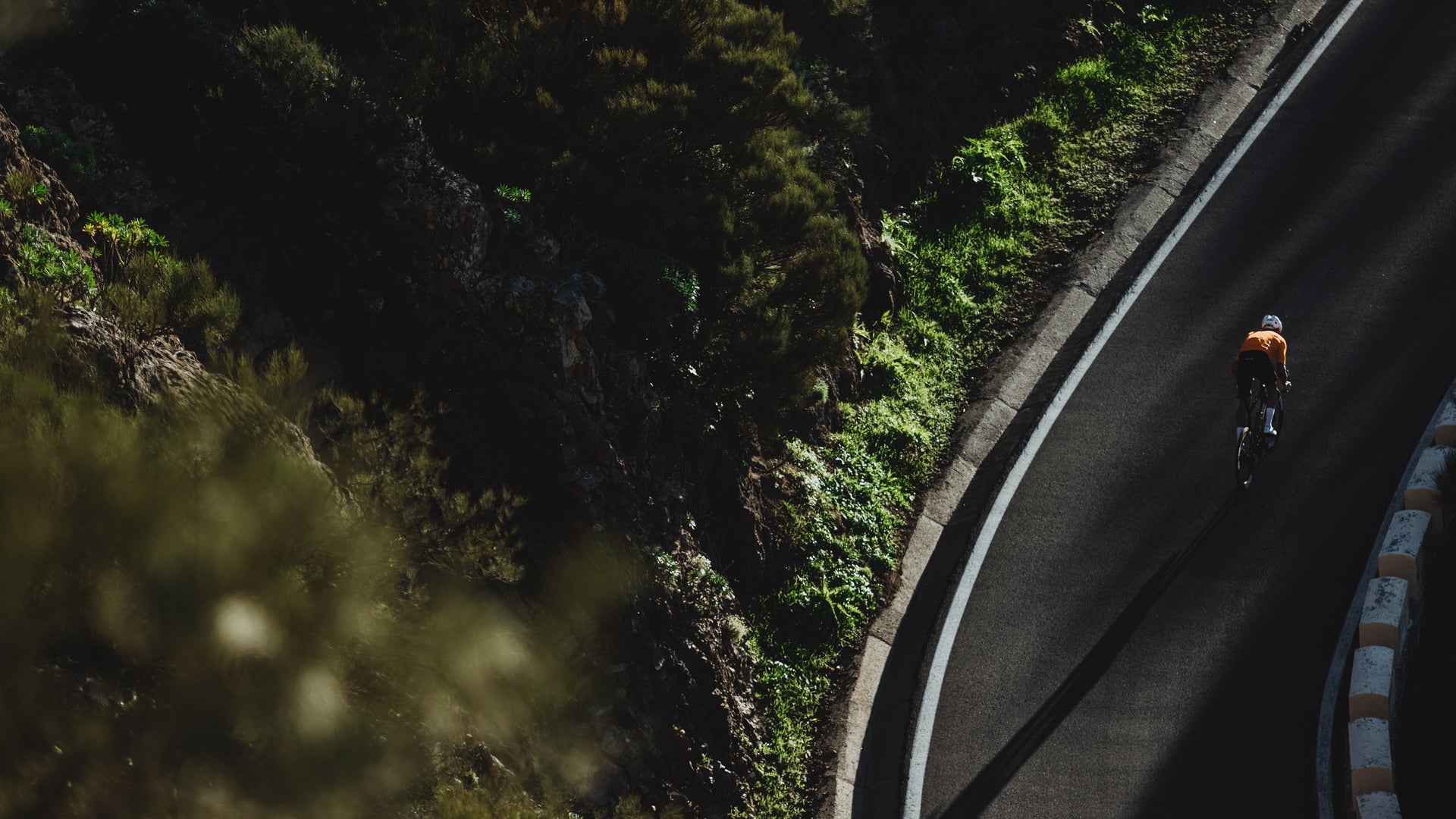 Birds eye view of one cyclist on a mountain road with planted mountain side