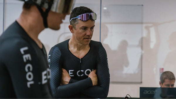 Lucas stood with arms crossed in Le Col Skinsuit in an office.