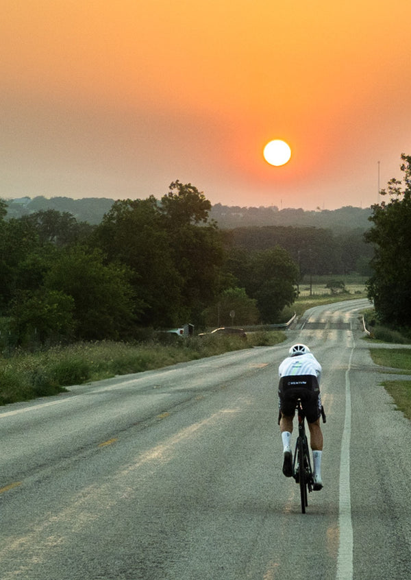 Cyclist riding downhill in countryside towards the setting sun
