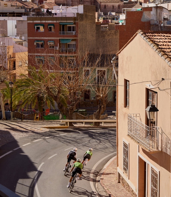 Aerial view of three cyclists veering round a road bend of a Valencia street.
