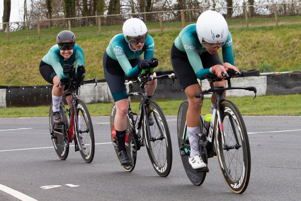 Three female cyclists in matching blue jerseys on racing bikes.