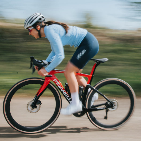 Female cyclists side profile riding in light blue long sleeved jersey and navy bibshorts
