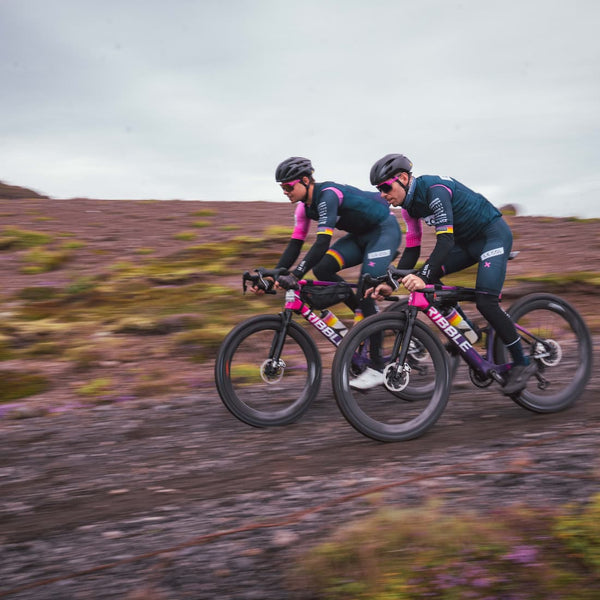 Two male cyclist racing head to head downhill on a flat rocky landscape.