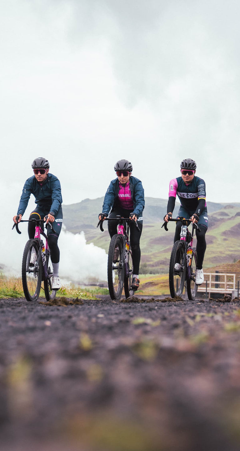 Four cyclists in matching pink jerseys riding on a road with a scenic background.