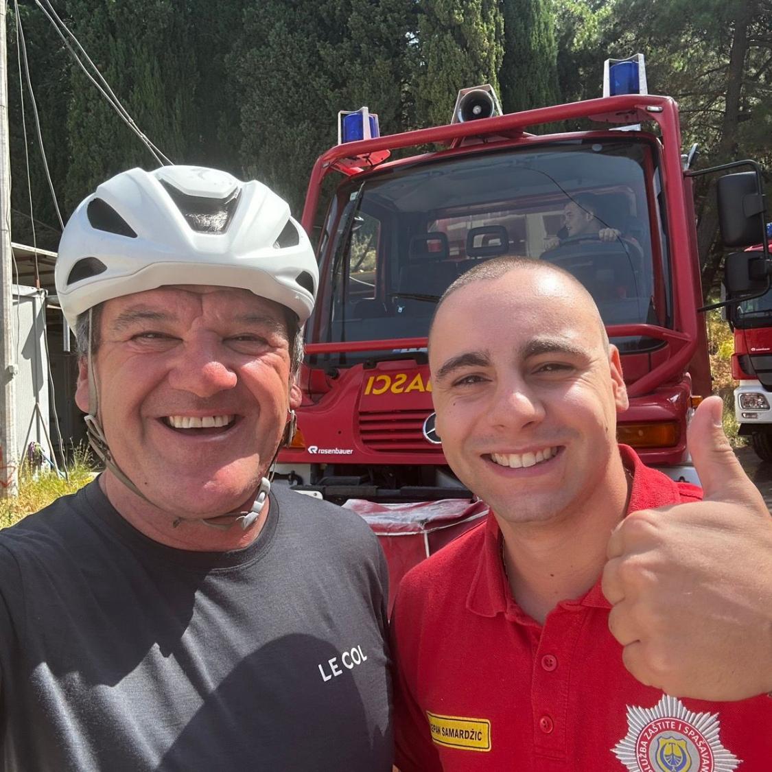 Two men standing in front of a red fire truck with trees in the background