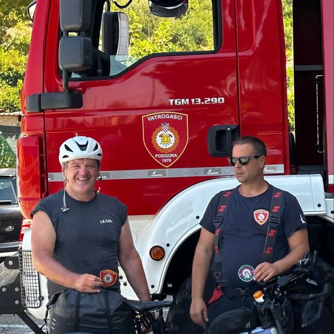 Two firefighters standing in front of a red fire truck with visible branding.