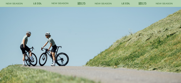 Male and female cyclist stopped by a grassy bank with a blue sky backdrop